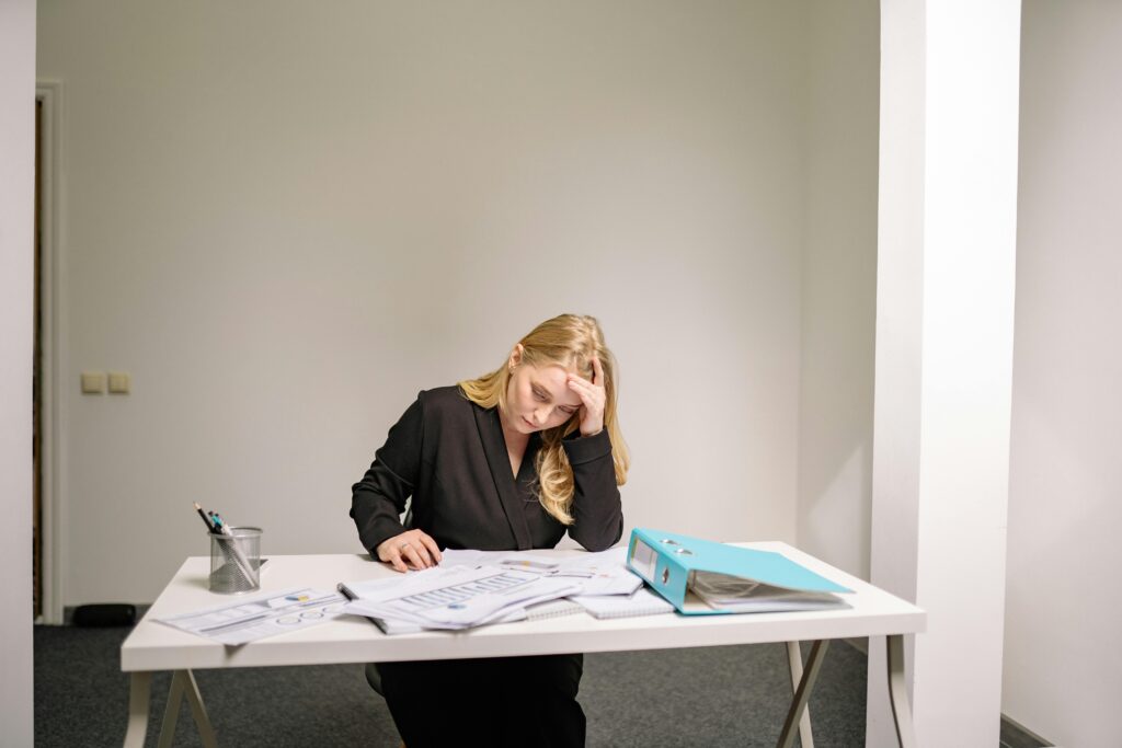 A stressed businesswoman reviewing documents at her desk, overwhelmed by paperwork.